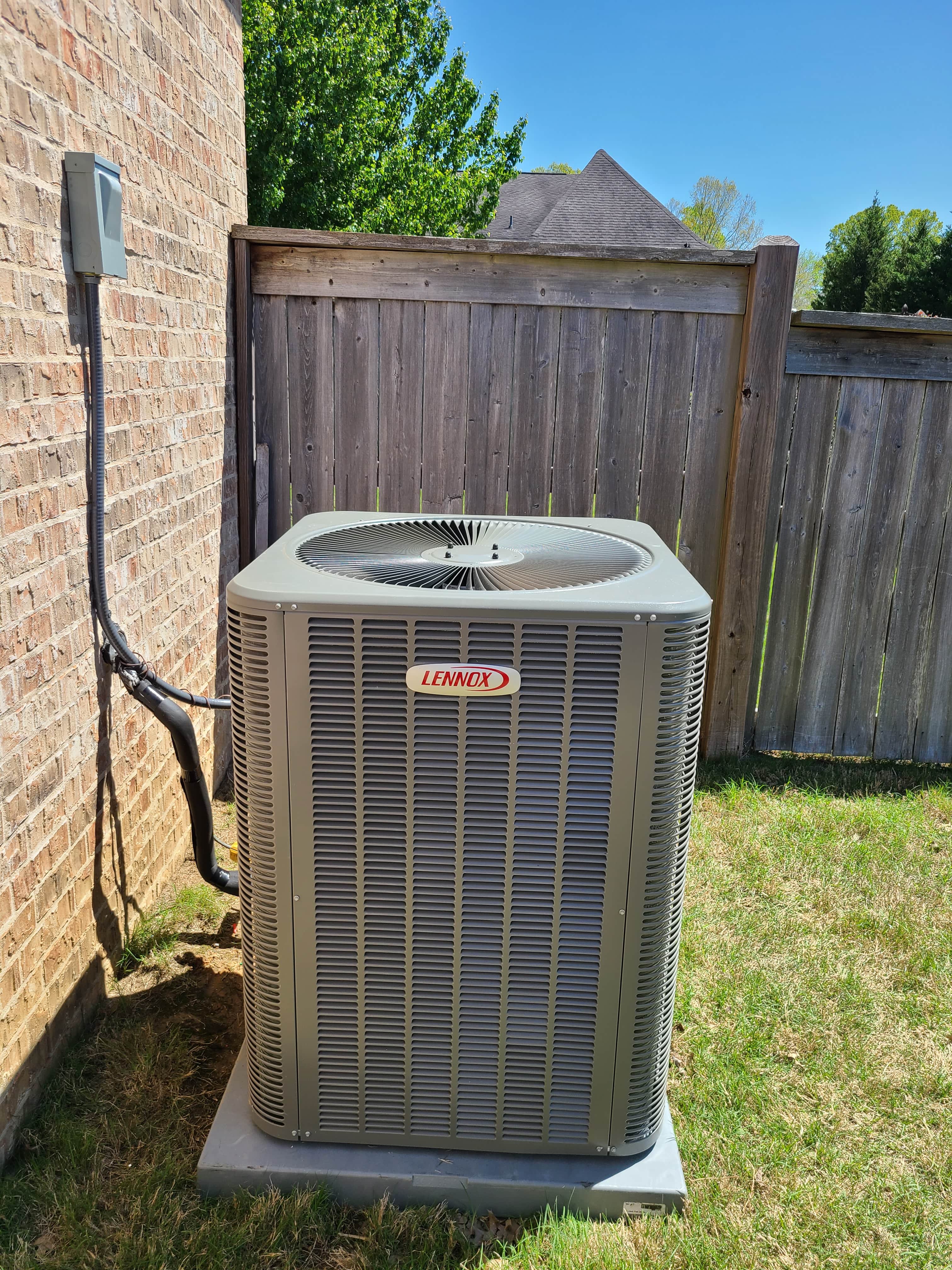 Outdoor air-conditioning unit beside a brick home and wooden fence